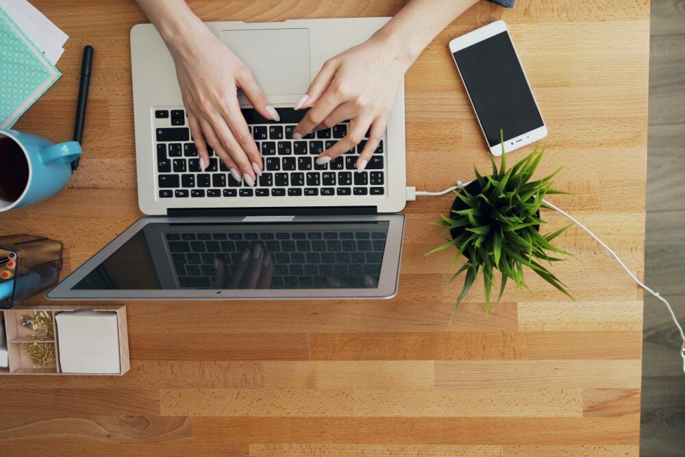 Desk surface with person typing on a laptop next to a plant