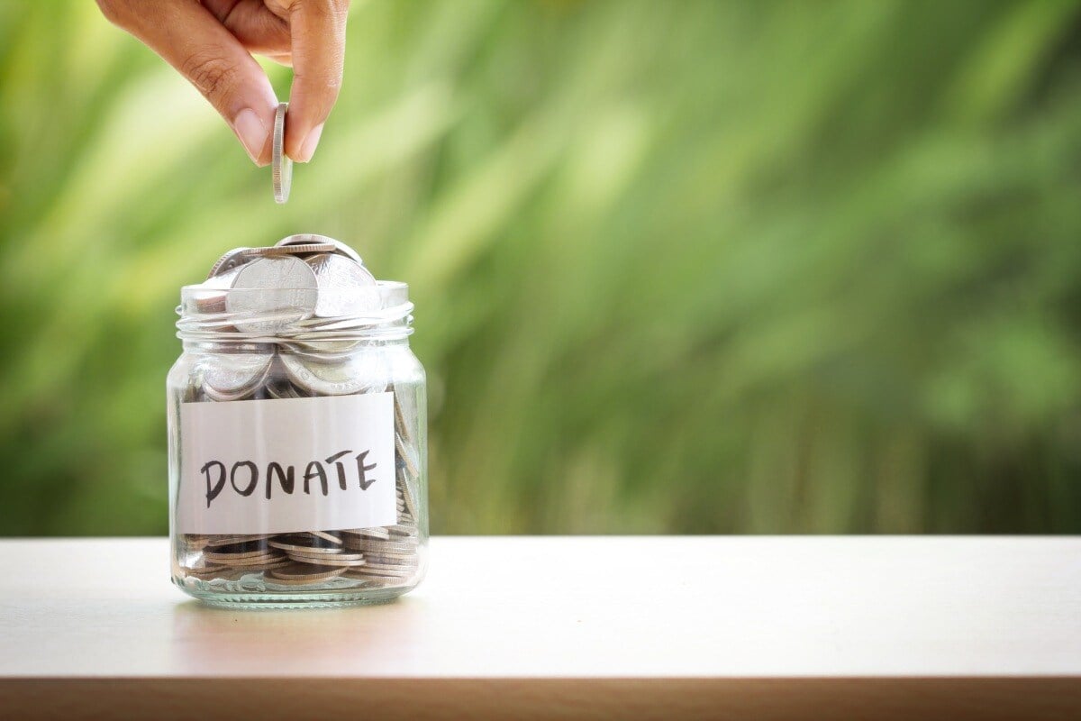 Hand putting a coin into a jar labeled Donate