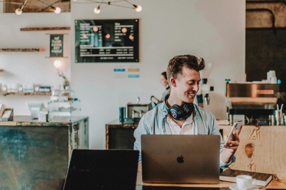 Man working at coffee shop with laptop and phone